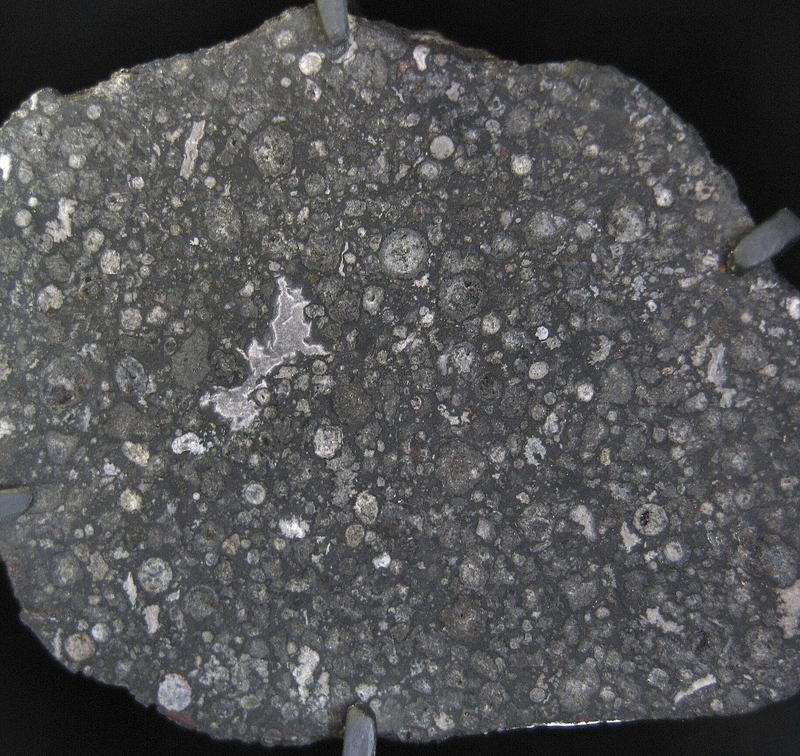Une tranche polie de la météorite Allende montrant des chondules arrondis de couleur claire incorporés dans une matrice sombre